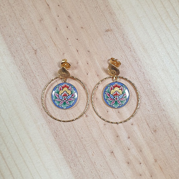 Boucles d'oreilles pendantes artisanales fleur orientale sur fond bleu.